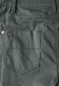 Mörkgrått tyg har ett bakfack med en sydd kontur och en liten metalltagg. Texturen verkar jämn och lätt.