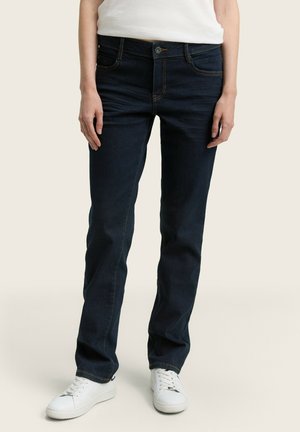 Mørke denimjeans med rett ben-design, kontrasterende oransje sømmer, fem lommer og knappeåpning, kombinert med hvite sneakers.