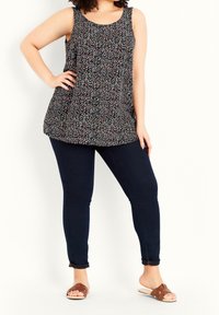 Schwarzes ärmelloses Oberteil mit einem floralen Muster in Weiß, Rot und Blau, kombiniert mit dunkelblauen Skinny Jeans und braunen Slippers.