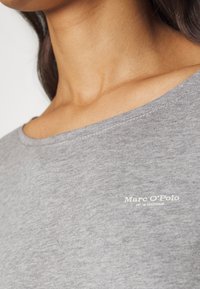 Szary bawełnowy t-shirt z szerokim dekoltem i białym napisem logo. Materiał ma teksturowany wygląd z subtelnymi wariacjami.