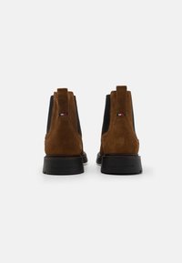 Bocanci de gleznă din suede maro cu panouri laterale de elastic negru, talpă plată neagră și cârlige la spate. Prezintă logo pe toc.