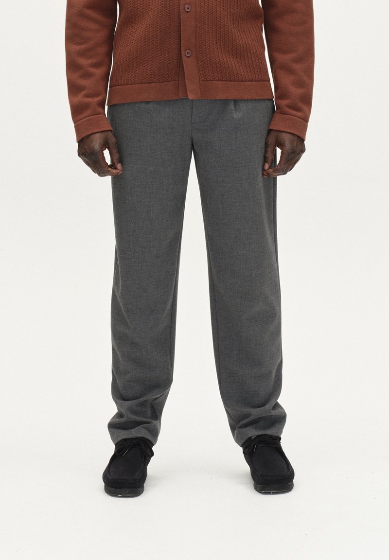 Hall-grå pükse, millel on peen tekstuur, on kombineeritud roostes värvi kudumisega kardiganiga, millel on nööbiga sulgemine, ja tumedate kingadega.