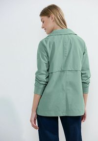 Chaqueta verde claro, de gran tamaño, con una parte trasera con yugo, cuello de solapa y mangas largas, hecha de un tejido suave y ligero.