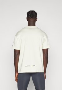 Cremefarvet t-shirt med korte ærmer i en afslappet pasform, der har adidas Terrex og National Geographic logoer ved bundkanten.