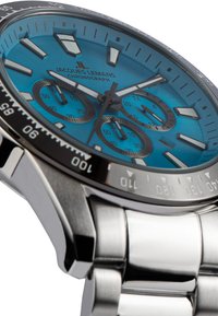 Kronografklocka med en turkos urtavla, silverfärgad rostfri stålkapsel och armband. Utrustad med svart bezel och tre sub-dialer för tidtagning.