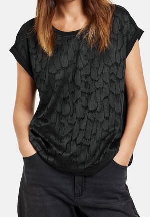 Top negro texturizado con mangas cortas, que presenta un patrón sutil, un ajuste relajado y un dobladillo curvo. Combinado con pantalones oscuros.