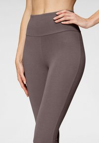Leggings elasticizzati a vita alta in un colore mauve tenue, caratterizzati da una trama del tessuto liscia e un design senza cuciture, senza hardware visibili.