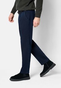 Marineblaue Hosen mit geradem Bein, ausgestattet mit seitlichen Taschen und slim fit, kombiniert mit schwarzen Wildleder-Stiefeletten.