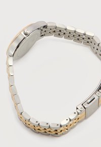 Μπρασελέ ρολογιού από ασημί και χρυσό μέταλλο με κούμπωμα και στρογγυλή θήκη ρολογιού, εμφανιζόμενο από πίσω σε λευκό φόντο.