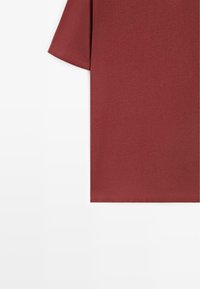 T-shirt à manches courtes, couleur rouille, uni, avec coutures visibles à l'ourlet, sur fond blanc.