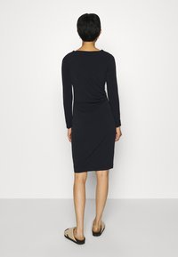 Långärmad klänning i mörk marinblått, tillverkad i mjukt tyg med en figurnära silhuett. Klänningen har en snodd detalj på baksidan och en knälång fåll.