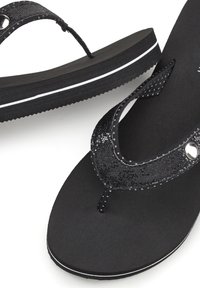 Black flip-flops with textured shiny straps, a flat sole with white accents, and a smooth matte finish. Lightweight and minimalist design.