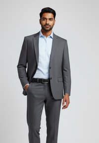 Grauer Anzug mit dezentem Muster, kombiniert mit einem hellblauen Hemd. Glatter Stoff, maßgeschneiderte Passform und ein schwarzer Gürtel vervollständigen den Look.