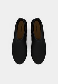 Pár černých nazouvacích bot s kulatými špičkami a hnědými stélkami označenými "PETER KAISER" na bílém pozadí.