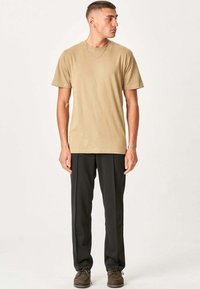 Beige bomulds t-shirt med en løs pasform, korte ærmer, parret med sorte, løstsiddende bukser og brune lædersko.