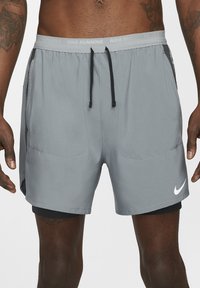 Sive kratke hlače za tek, izdelane iz lahkega materiala, z elastičnim pasom na vrvico, stranskimi žepi in črnimi detajli. Na robu je logotip Nike.