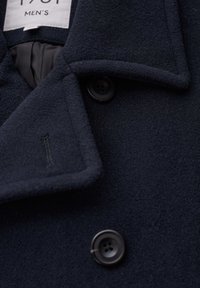 Cappotto da uomo blu navy in lana con colletto a rever, due grandi bottoni neri e un tessuto morbido e testurizzato.