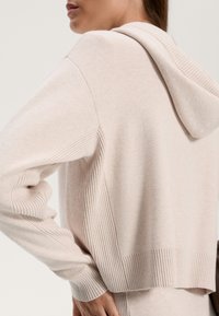 Felpa cropped rosa chiaro realizzata in morbido tessuto, con texture a coste sulle maniche e sull'orlo, dotata di cappuccio centrale e vestibilità rilassata.
