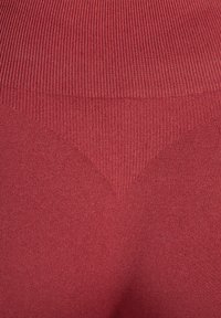 Tissu tricoté rouge avec texture côtelée, présentant un motif triangulaire près du centre, fini lisse et apparence douce.