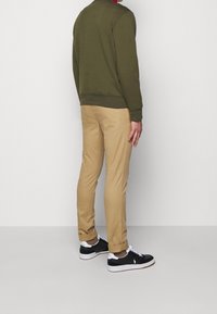 Olivgrön sweatshirt, beige tapered byxor och svarta sneakers med vita detaljer. Slät tyg, ribbat manschett och uppvikt byxkant.