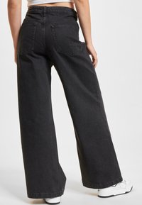 Blugi negri cu croială largă, din denim. Au talie înaltă, două buzunare în spate și un design curat, simplu. Purtați cu adidași albi.