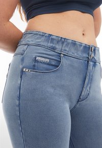 Högmidjade blå denimbyxor med en lätt blekt finish, två knäppningar, en framficka och dekorativa rhinstenar på fickan.