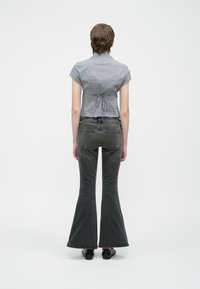 Κοντή μπλούζα με καρό μοτίβο και κοντά μανίκια, με σφικτή μέση. Ανοιχτόχρωμο γκρι τζιν με φαρδιά γραμμή, πίσω τσέπες και λείο υλικό. Μαύρα παπούτσια.