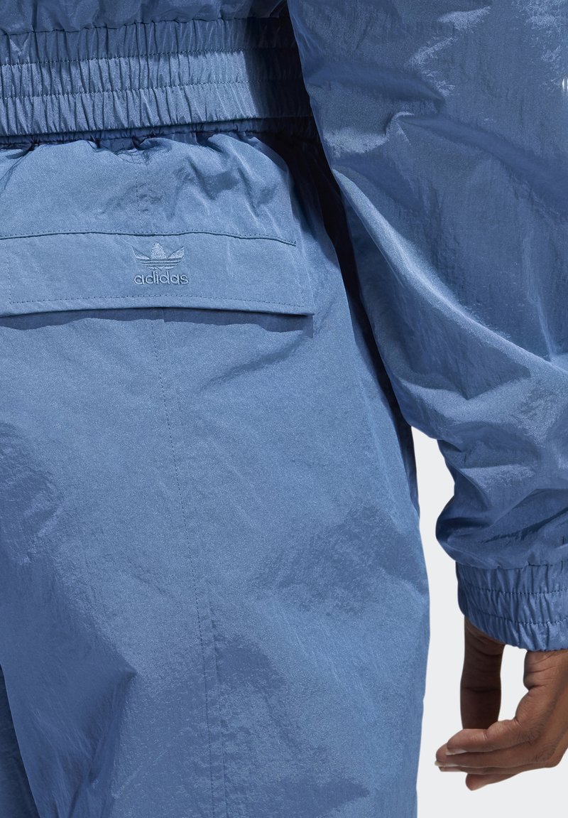 Lichtblauwe windjack met elastische tailleband, textuurstof en een klein adidas-logo op de achterzak. Soepel, modern ontwerp.