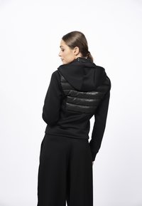 Czarna bluza z kapturem z teksturowaną, puszystą wstawką na plecach, z kapturem i dopasowanymi rękawami. Miły w dotyku materiał, elegancki design i minimalistyczny styl.