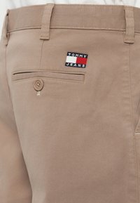 Beezid püksid, millel on nööbiga tagatasku ja väike Tommy Jeansi logo paigatud tasku kohal.