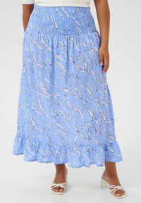 Lichtblauwe rok met een golvend bruin patroon, voorzien van een smocktail en een gerimpelde zoom. Gecombineerd met witte hakken sandalen.
