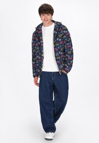 Hooded jack in marineblauw met multicolor gaminggraphics; wit t-shirt en losse denim jeans. Model draagt witte sneakers.