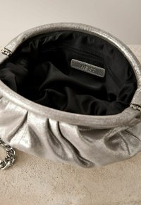 Silberne, metallische Handtasche mit gepuffter Textur, schwarzem Innenfutter, Reißverschlusstasche und einer Kettenriemen. Innenetikett sichtbar.