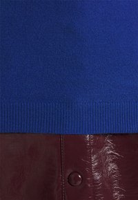 Niebieski sweter z dzianiny z prążkowanym dołem w połączeniu z błyszcząca burgundową skórzaną spódnicą z wyraźnym detalem guzikowym.