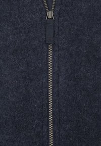 Marineblauwe wollen zip-up jas met een zilveren metalen rits, een gestructureerd oppervlak en tonale stitching. De rits loopt centraal aan de voorkant.