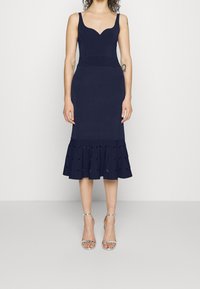 Robe ajustée bleu marine avec un décolleté en cœur et un ourlet évasé à volants avec des détails découpés. Tissu lisse et design soigné.