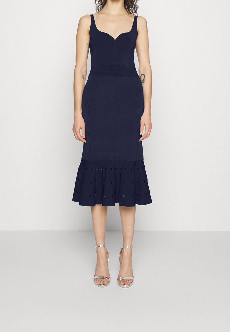 Robe ajustée bleu marine avec un décolleté en cœur et un ourlet évasé à volants avec des détails découpés. Tissu lisse et design soigné.