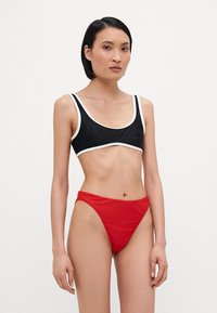 Top de bikini negru cu tiv alb și fund de bikini înalt, roșu. Materialul pare neted și elastic, proiectat pentru a fi utilizat ca îmbrăcăminte de baie.