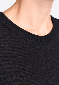 Schwarzer, gerippter Strickstoff mit einem enganliegenden Rundhalsausschnitt. Die Textur wirkt leicht reflektierend und hat eine glatte Oberfläche.