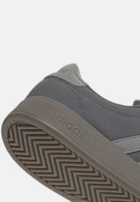 Primo piano di una sneaker grigia Adidas che mostra la suola in gomma testurizzata con motivo a spina di pesce e la parte superiore in tessuto con accenti di suede.