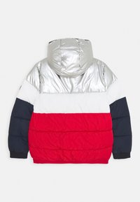 Vadderad jacka med en glänsande silverhuva, med röda, vita och marinblå horisontella ränder. Strukturerat tyg med elastiska ärmslut.
