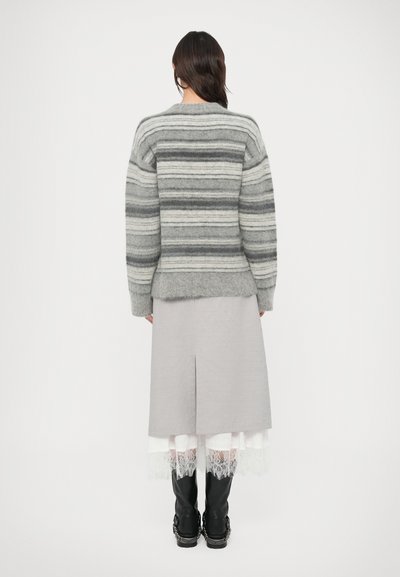 Hall triibuline villane kampsun, millel on kastikujuline lõige ja sooniline tekstuur. Sobitatud halli seelikuga, millel on pitsiline ääris. Mustad saapad.