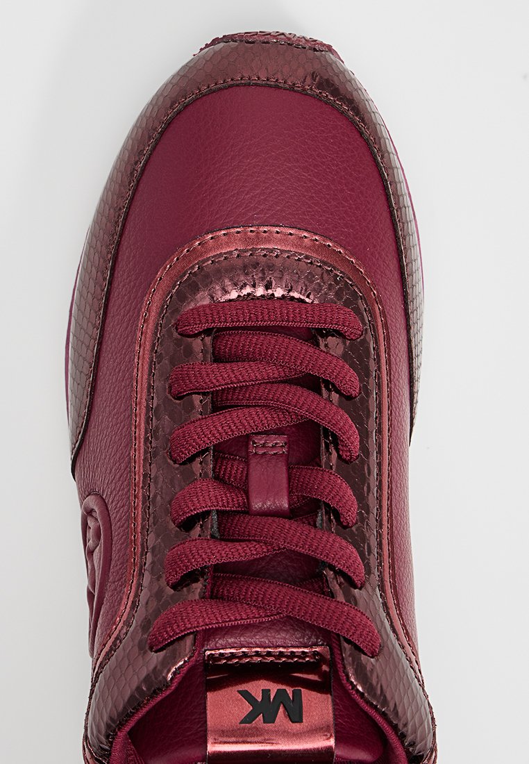 Sneaker bordeaux in pelle e tessuto texture, con lacci coordinati e dettagli metallici con logo "MK" impresso sulla linguetta.