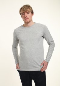 Světle šedé tričko s dlouhým rukávem z jemné, hladké látky s kulatým výstřihem. Střih je volný, s rovnými rukávy a bez vzorů.