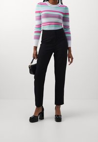 Pullover a righe e coste in colori pastello, abbinato a pantaloni neri a gamba dritta a vita alta e scarpe con plateau nere lucide.