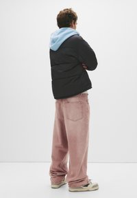 Sort pufferjakke med blå hætte, lys pink oversized jeans og beige sneakers med grønne accenter. Teksturstof og afslappet pasform.