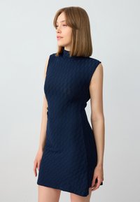 Marineblauwe mouwloze jurk met een hoge halslijn, voorzien van een gestructureerd geometrisch patroon en een aansluitende silhoeet.