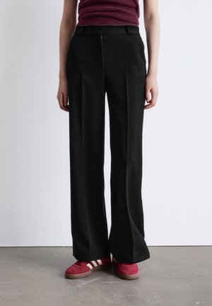 Wide-leg black trousers made of woven fabric, featuring a tailored design, front pleats, and a zip closure, paired with red sneakers.