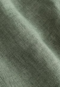 Gros plan d’un tissu vert tissé montrant une texture détaillée et des plis subtils.