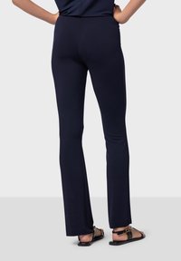 Marinblå, figurnära byxor med en jämn textur, utsvängd design och hög midja, kombinerat med svarta sandaler med ett guldakcent.